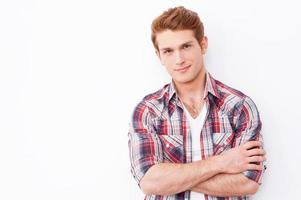 charmant beau. beau jeune homme gardant les bras croisés et regardant la caméra en se tenant debout sur fond blanc photo