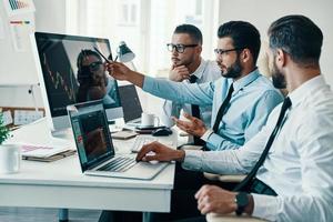 compte tenu de la prochaine étape. groupe de jeunes hommes modernes en tenues de soirée analysant les données boursières tout en travaillant au bureau photo