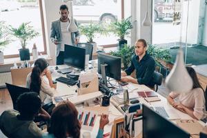 groupe de jeunes gens modernes en vêtements décontractés intelligents communiquant et utilisant des technologies modernes tout en travaillant au bureau photo