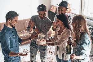 joyeux anniversaire vue de dessus d'un jeune homme heureux célébrant son anniversaire entre amis tout en se tenant dans la chambre avec des confettis volant autour photo