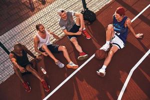 Fatigué mais heureux. vue de dessus de jeunes hommes en tenue de sport souriant assis sur le terrain de basket à l'extérieur photo