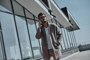 toujours en contact. sérieux jeune homme moderne parlant au téléphone intelligent tout en se tenant à l'extérieur photo