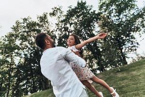 profiter de chaque minute ensemble. jeune père aimant portant sa fille souriante tout en passant du temps libre à l'extérieur photo