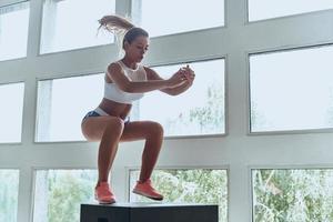 toujours en forme. jeune femme moderne en vêtements de sport sautant pendant l'exercice dans la salle de gym photo