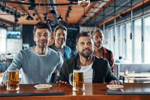 jeunes hommes excités en vêtements décontractés buvant de la bière et regardant un match de sport assis dans le pub photo