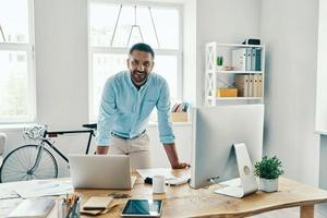 bel homme d'âge moyen en tenue décontractée intelligente regardant la caméra et souriant tout en se tenant au bureau photo