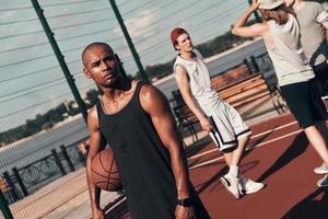 une autre pause. jeune homme africain en vêtements de sport regardant loin tout en jouant au basket-ball à l'extérieur photo