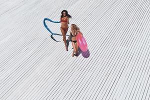 vous ne pouvez jamais avoir trop d'été. vue de dessus pleine longueur de deux belles jeunes femmes en bikini souriant tout en courant à l'extérieur photo