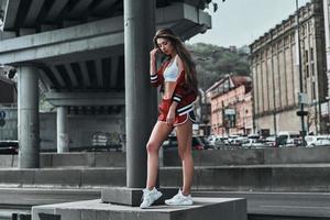 en forme et belle. toute la longueur d'une jeune femme séduisante en vêtements de sport touchant les cheveux avec la main tout en posant sous le pont à l'extérieur photo