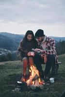 nuit romantique. beau jeune couple dégustant des boissons chaudes tout en se réchauffant près du feu de camp dans les montagnes photo