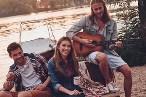 pas de transport et de précipitation. groupe de jeunes en tenue décontractée souriant tout en profitant d'une fête sur la plage près du lac photo