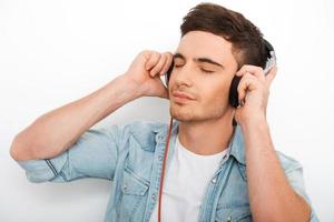 profiter de la bonne musique. beau jeune homme dans les écouteurs en gardant les yeux fermés en se tenant debout sur fond blanc photo