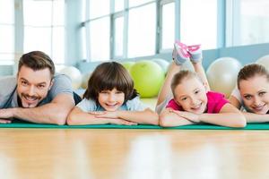 famille sportive heureuse. famille heureuse se liant les unes aux autres en position allongée sur un tapis d'exercice dans un club de sport photo