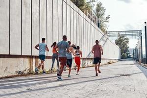 vue arrière sur toute la longueur des jeunes en vêtements de sport faisant du jogging tout en faisant de l'exercice sur le trottoir à l'extérieur photo