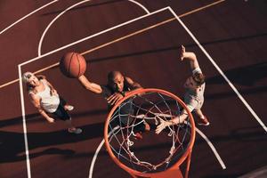 prêt à marquer. vue de dessus d'un jeune homme en vêtements de sport marquant un slam dunk tout en jouant au basket avec des amis à l'extérieur photo