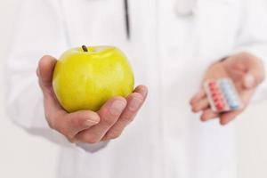 le bon choix. médecin senior cheveux gris en uniforme tenant une pomme dans une main et des pilules dans une autre tout en se tenant isolé sur blanc photo