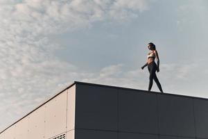 elle est en forme. toute la longueur d'une jeune femme moderne en vêtements de sport marchant tout en passant du temps sur le toit à l'extérieur photo