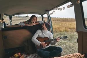 beau jeune homme jouant de la guitare pour sa belle petite amie tout en étant assis dans un mini van de style rétro photo