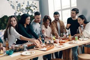 délicieuses pizzas. groupe de jeunes en tenue décontractée mangeant de la pizza et souriant tout en dînant à l'intérieur photo