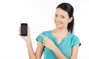 femme avec téléphone portable. joyeuse jeune femme tenant un téléphone portable et le pointant tout en étant isolé sur blanc photo