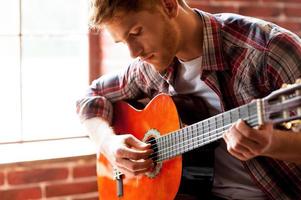 bel homme jouant de la guitare. gros plan sur un jeune homme jouant de la guitare acoustique assis devant la fenêtre photo