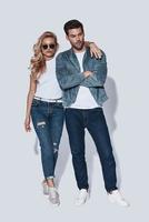 jeune et confiant. toute la longueur du beau jeune couple en vêtements de denim embrassant en se tenant debout sur fond gris photo