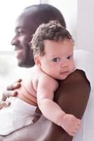 papa fier et heureux. heureux jeune homme africain tenant son petit bébé et souriant tout en se tenant près de la fenêtre photo