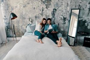 vous pouvez tout trouver en ligne. beau jeune couple utilisant une tablette numérique tout en passant du temps au lit à la maison photo