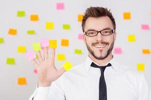 entreprise créative. joyeux jeune homme en tenue de soirée tenant des notes adhésives sur ses doigts et souriant tout en se tenant contre le mur avec de nombreuses notes adhésives dessus photo