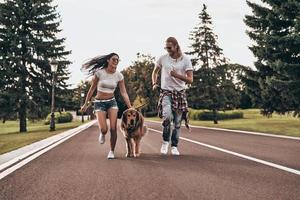 belle journée dans le parc. toute la longueur d'un beau jeune couple courant avec son chien tout en passant du temps à l'extérieur photo