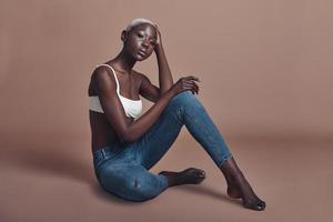 magnifique modèle sensuel. séduisante jeune femme africaine regardant la caméra assise sur fond marron photo