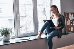 envisager la prochaine étape. jeune femme concentrée travaillant assise sur le rebord de la fenêtre du bureau photo