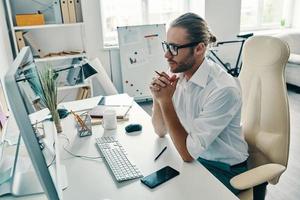 envisager la prochaine étape. vue de dessus d'un jeune homme réfléchi en chemise travaillant à l'aide d'un ordinateur assis au bureau photo