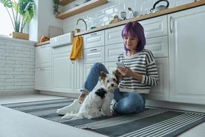 jeune femme passant du temps avec son chien tout en utilisant le téléphone et assise par terre à la cuisine photo