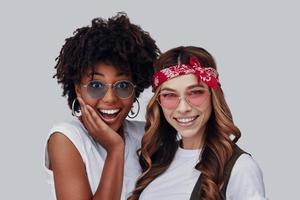 deux jolies jeunes femmes regardant la caméra et souriant en se tenant debout sur fond gris photo