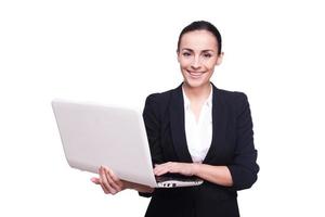 confiant dans son ordinateur portable. belle jeune femme en tenues de soirée travaillant sur ordinateur portable isolé sur fond blanc photo