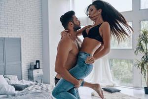 appréciant chaque minute ensemble. beau jeune homme torse nu portant une femme séduisante semi-habillée debout dans la chambre photo