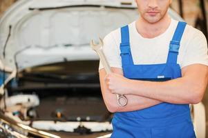 prêt à travailler. gros plan sur un jeune homme confiant tenant une clé en se tenant debout dans un atelier avec une voiture en arrière-plan photo