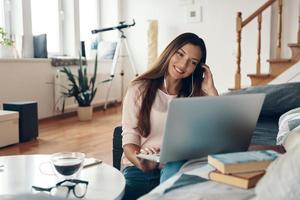 jolie jeune femme en vêtements décontractés parlant à quelqu'un utilisant un ordinateur portable tout en se reposant à la maison photo