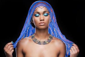 trop beau pour être vrai. belle femme africaine couvrant la tête par un foulard et gardant les yeux fermés en se tenant debout sur fond noir photo