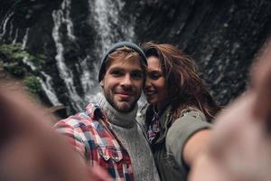 autoportrait d'un beau jeune couple souriant debout à l'extérieur avec la cascade en arrière-plan photo