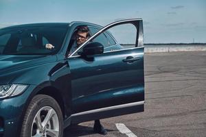 voiture de luxe. beau jeune homme en vêtements d'affaires entrant dans sa voiture photo