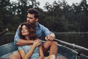 aimer tout d'elle. beau jeune couple embrassant et regardant ailleurs tout en profitant d'un rendez-vous romantique sur le lac photo