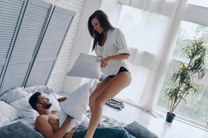 se sentir libre de tout faire. heureux jeune couple ayant une bataille d'oreillers amusante tout en passant du temps sans soucis dans la chambre photo