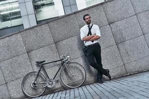 meilleur transport urbain. beau jeune homme en costume complet en gardant les bras croisés et en détournant les yeux tout en se tenant à l'extérieur photo