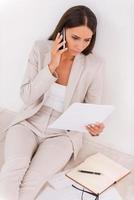 occupé par le travail. vue de dessus d'une jeune femme d'affaires confiante examinant un document et parlant au téléphone portable tout en étant assis sur le sol photo