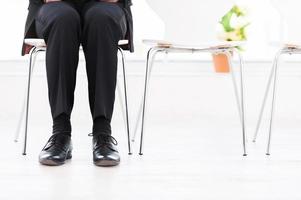 en attente d'entretien. image recadrée d'un homme en tenues de soirée assis à la chaise avec d'autres chaises debout dans une rangée photo