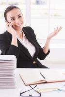 femme d'affaires heureuse. heureuse jeune femme en tenues de soirée parlant au téléphone portable alors qu'elle était assise sur son lieu de travail photo