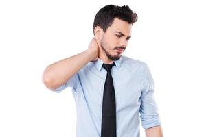 sensation de douleur dans le cou. jeune homme frustré en chemise et cravate touchant son cou et exprimant la négativité en se tenant debout sur fond blanc photo