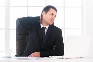 malade et fatigué. jeune homme frustré en tenues de soirée regardant ailleurs et touchant son cou avec la main alors qu'il était assis sur son lieu de travail photo